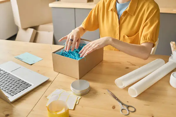 Close-up of woman packing parcel for delivery sitting at table in front of laptop to work with online orders