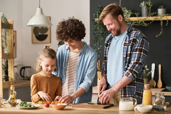 Happy parents teaching their son to prepare salad for dinner while standing at table in kitchen