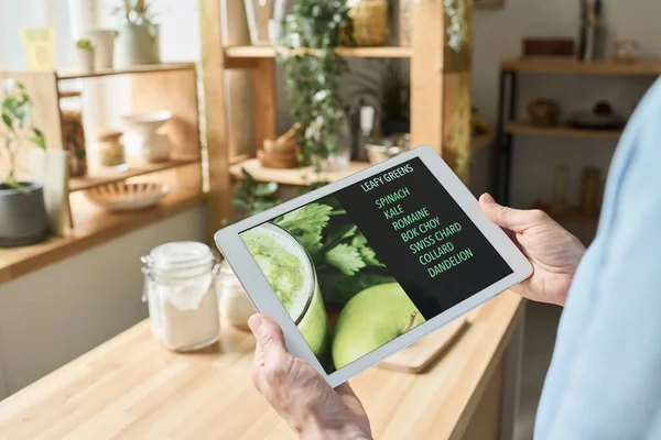 Close-up of woman using digital tablet to read recipe of fresh healthy cocktail while standing in kitchen