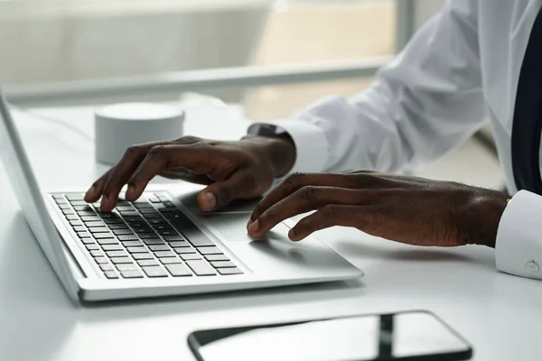 Close-up of African American businessman typing on laptop and doing his online work at table at office