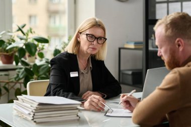 Sigorta bürosundaki yetişkin kadın danışman erkeğin portresi ve başvuru formlarına işaret etmek