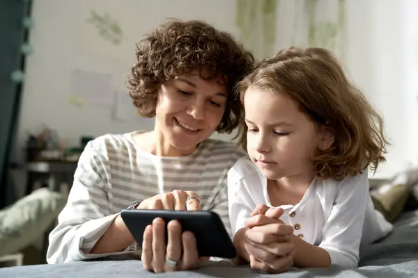 Smiling mother showing video on smartphone to her child during their leisure time at home