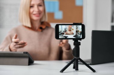 Tripodun üzerinde ayakta duran akıllı telefonun yakın plan fotoğrafı. Sınıftaki öğrencileri için öğretmeninin online dersi var.