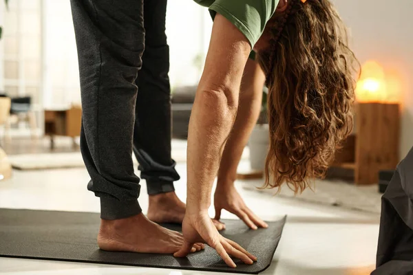 Close-up of barefoot man standing on exercise mat and doing stretching exercises