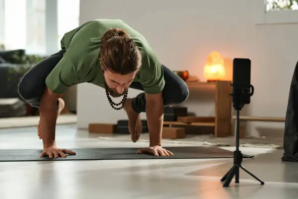 Young man making yoga pose on exercise mat and shooting it for his blog online