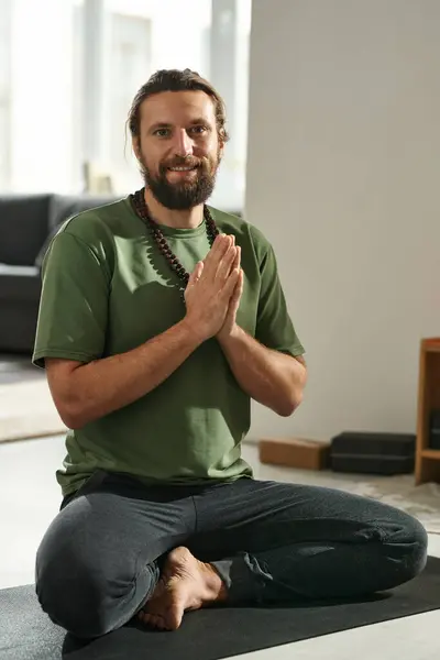 Portrait of happy man meditating in lotus position on exercise mat and smiling at camera