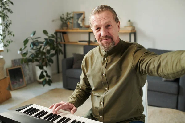 Mature bearded man looking at camera while teaching to play piano online