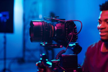 Genç Afrikalı Amerikalı kameraman profesyonel kamerayla çalışıyor ve stüdyoda çekim yapıyor.