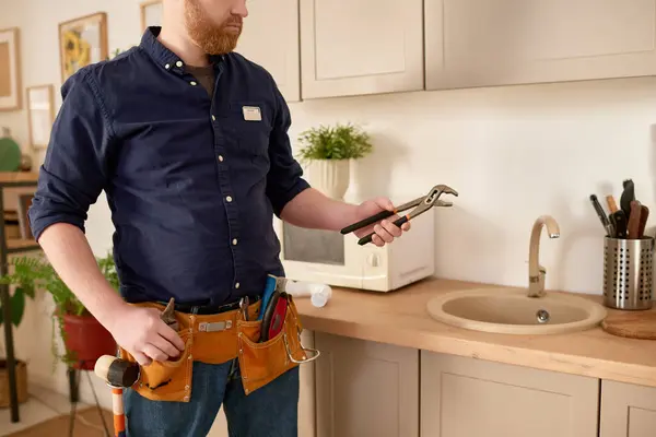 Repairman with belt with work tools using wrench to repair sink in domestic kitchen