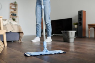 Ev hanımı odada ev işi yaparken yakın plan çekimde yerleri silmek için paspas kullanıyor.