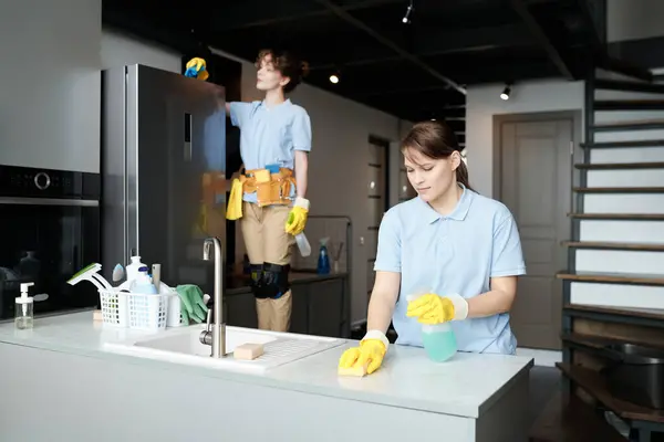Ev işleri sırasında takımda çalışan genç kadınlar, mutfaktaki mobilyaların tozunu silerler.