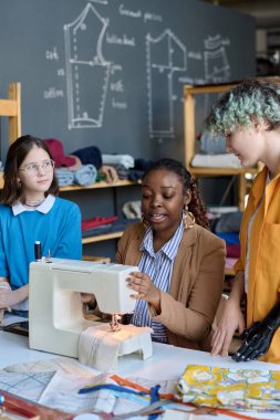 Afrika kökenli Amerikalı bir kadının dikey portresi. Atölyede engelli kızlara akıl hocalığı yapıyor. Dikey dikiş teknikleri gösteriyor.