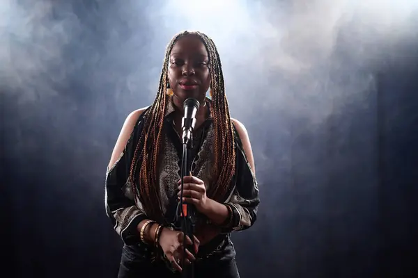 Waist up portrait of Black young woman with braided hair standing on stage with smoke background ready for performance copy space