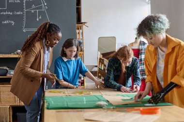 Atölye atölyesindeki terzilik sınıfındaki çeşitli kızlar ve siyahi bir kadın mekanın kopyalanmasına yardım ediyor.