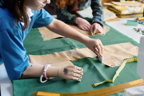 Cropped shot of girl with prosthetic arm making clothing and tracing patterns in sewing class copy space