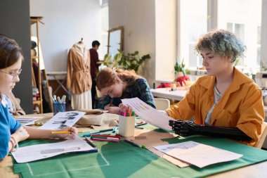 Inclusive group of girls drawing clothing sketches in tailoring class at table clipart