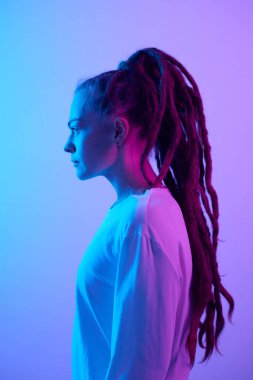 Uzun saçlı, mavi ve mor neon ışıklı beyaz bir kadının dikey yan görünüşlü portresi