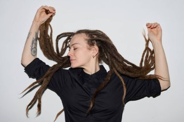 Beyaz arka planda flaşla dans eden, uzun rastalı beyaz kadın portresi