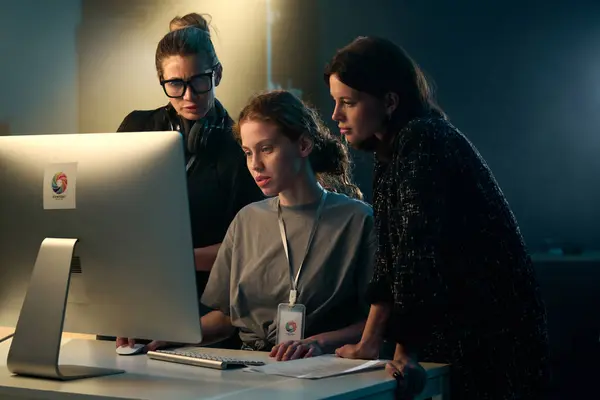 三个女人在背光视频制作装置上一起看电脑屏幕的极小镜头 免版税图库照片