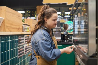 Side view portrait of independent adult woman with Down syndrome working with oven in cafe or bakery