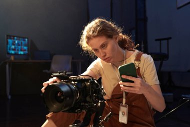 Kadın yaratıcının arka ışıklandırılmış portresi, dijital video kamerayı altın rengi telefon ile kuruyor, boşluğu kopyala