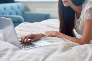 Genç bir kadının laptopta sosyal ağlarını kullanmasına ve yatakta yatmasına yakın çekim.