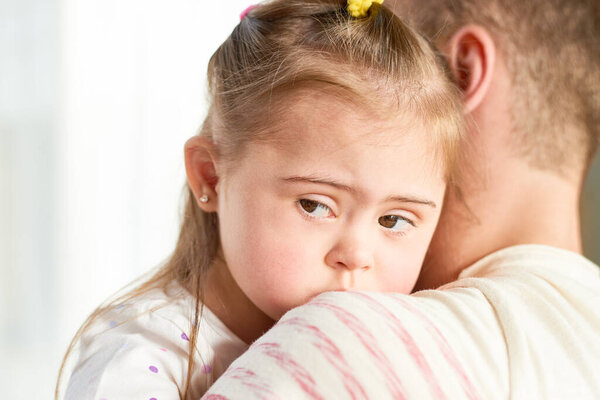 Крупный план отца, держащего милую маленькую дочь с синдромом Дауна, смотрящего в сторону от камеры, копирующего пространство