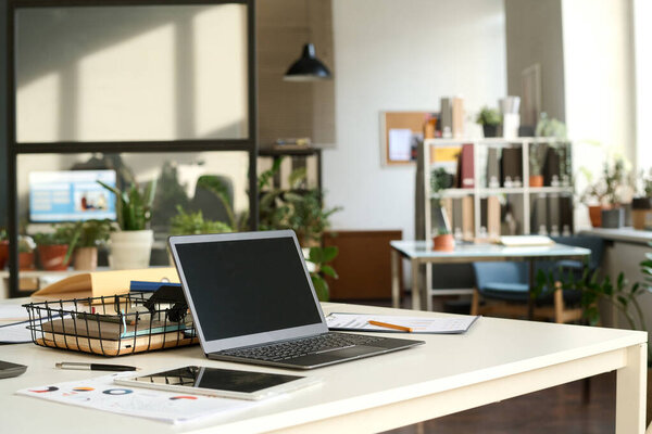 Background image of sunlit open office interior with laptop on workplace desk in focus, copy space