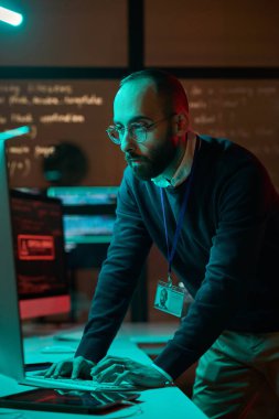 Mavi neon ışıklarda bilgisayar ağı ile çalışan sakallı siber güvenlik mühendisinin dikey portresi