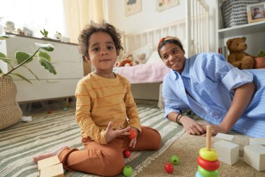 Anne, oyuncaklarla ve oyuncak doldurulmuş hayvanlarla dolu yerde oturmuş oyun odasında aile bağları ve eğlenceli aktiviteler kuruyor.