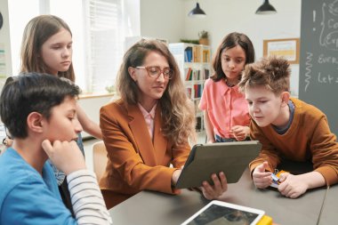Sınıfta bir grup çocukla tablet kullanan gülümseyen kadın öğretmen portresi.