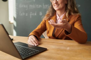 Yan görüntüde gülümseyen bayan öğretmenin görüntüsü el hareketlerine odaklanıyor.