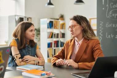 Okul kütüphanesinde danışmanlık sırasında engelli bir kızla konuşan ilgili kadın öğretmen portresi.