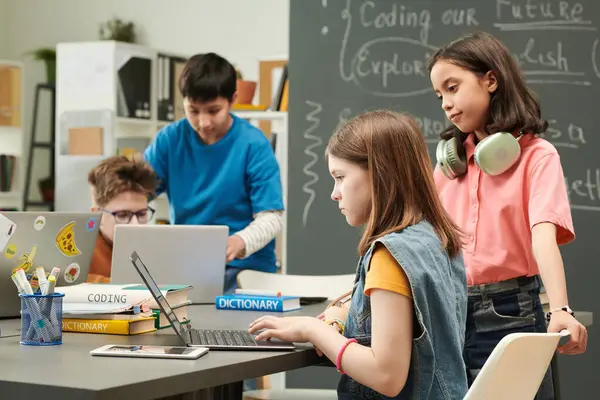 Okul kütüphanesinde bilgisayar kullanan ve ön planda fotokopi alanındaki iki kıza odaklanan çocukların renkli portresi