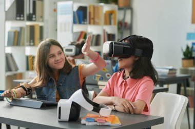 Okulda sanal gerçeklik teknolojisi kullanan gülümseyen iki genç kızın portresi çocuklar için bilgisayar dersinden zevk alıyor.