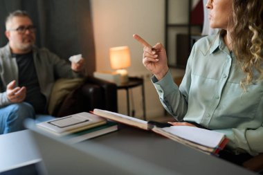 Ofis toplantısı sırasında masada oturan meslektaşlar stratejik tartışmalara giriyorlar. Arka planda elinde kahve fincanı olan bir adam, önünde kalemle el kol hareketi yapan bir kadın.