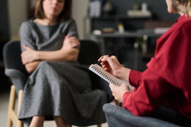 Hasta kollarını kavuşturup huzurlu bir ortamda endişelerini dile getirirken psikologların not aldığı profesyonel danışmanlık seansı.