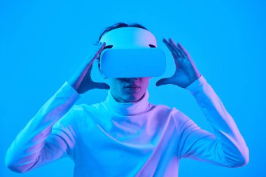 Sanal gerçeklik deneyimine dalmış mavi monokromatik arka planda VR kulaklık takmış ileri teknoloji atmosferini tasvir eden biri.