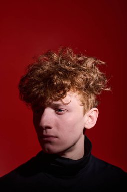 Kıvırcık saçlı, parlak kırmızı arka planda düşünceli genç bir adam, gölge düşürüyor. İnsan kameradan hafifçe yüz çevirdi, dramatik ve içsel bir ruh hali yarattı.