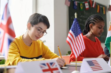 Okul sınıfındaki uluslararası konferans sırasında masada Amerikan bayrağıyla oturan genç kız portresi.