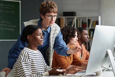 Modern sınıf ortamında öğrencilerin odaklandığı bilgisayarlardan aktif olarak öğrenim gördükleri çeşitli sınıf ortamlarında çeşitli öğrencilere yardım eden eğitimci