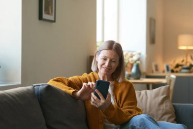 Akıllı telefon kullanan ve sosyal medyayı kaydıran gülümseyen olgun bir kadının portresi.