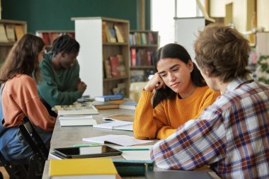 Üniversite kütüphanesi çalışma alanında birlikte okuyan bir grup kolej öğrencisi sohbete katılıyor ve notlarını paylaşıyorlar. Kitaplar ve cihazlar masanın etrafına konur.