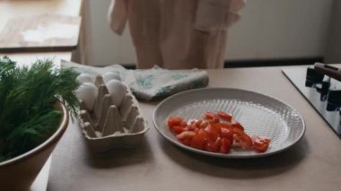 Tanımlanamayan bir kadının taze domatesleri zarif tabağa sererken sıcak mutfağında ahşap tezgahlarla kendisine sağlıklı bir yemek hazırlarken görüntüsü.
