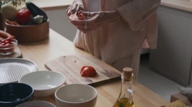 Ahşap mutfak tezgahında, elinde şef bıçağıyla taze, sulu domatesleri tahta tahtayla keserken çekilmiş görüntüler.