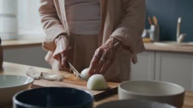 Tanınmayacak haldeki rahat keten giysili bir kadının, ahşap mutfak tezgahında soğan soyarken sağlıklı bir öğle yemeği hazırlarken görüntüsü.