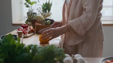 Tanımlanamayan bir kadının, şefin bıçağıyla biber keserken sıcacık mutfakta sağlıklı bir yemek hazırlarken çekilmiş yan görüntüsü.