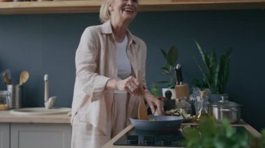 Kafkasyalı olgun bir kadının rahat mutfağında taze pişmiş yemeğini tatmak ve koklamak için eğildiği, etrafını bitki ve çatal bıçaklarla sardığı, sonra da tadı değerlendirmek için karabiber eklediği bir fotoğraf.