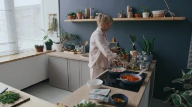 Orta boy Kafkasyalı kadın tuzlu ve biberli kıyma ile baharatlı et pişirirken endüksiyon sobasında tavada kızartırken sıcacık, evcil mutfak ortamında lezzetli yemekler pişirirken.