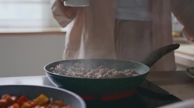 Tanımlanamayan bir kadının tuzlanmış eti tuzlayıp tavaya domates püresiyle kızartıp modern mutfakta ev yapımı Bolonez yapması.